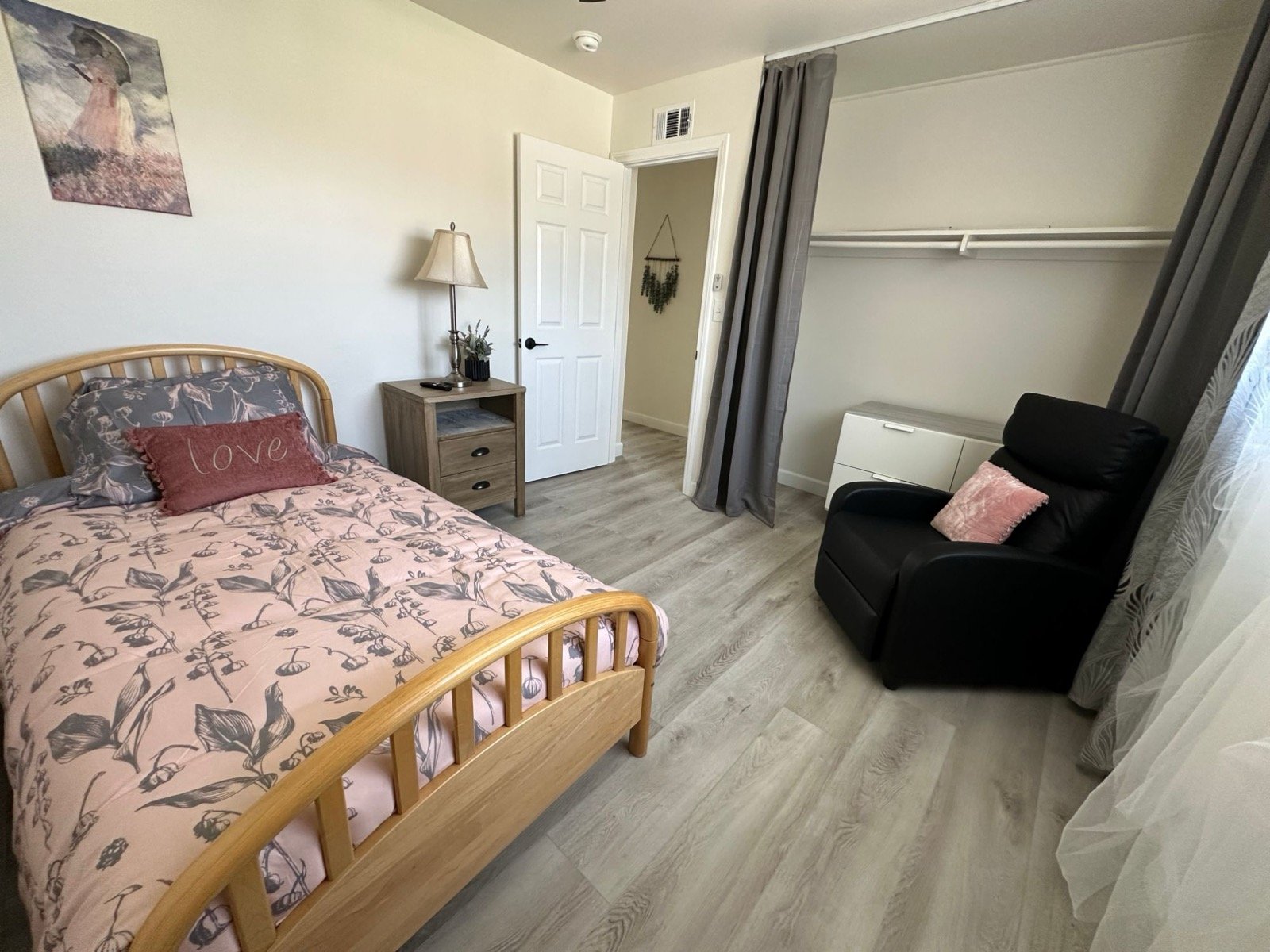 Private bedroom with pink floral bedding, nightstand and recliner