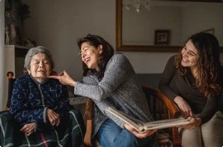 Family members laughing with an elderly woman as they share a photo album